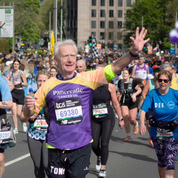 Male runner running in the TCS London Marathon, waving to the crowd