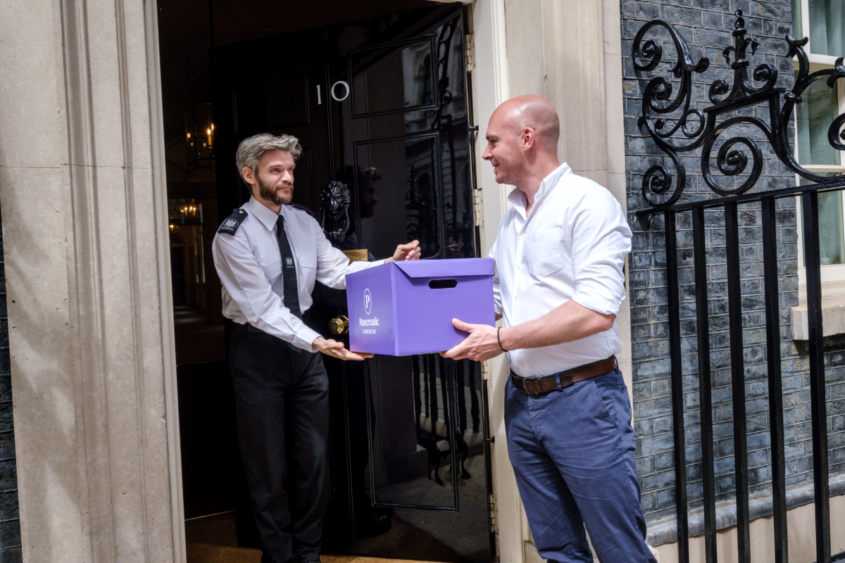 man wearing a white shirt handing a box to a officer at downing street