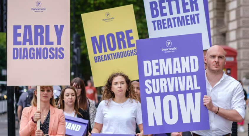 group of people marching towards Downing Street, holding signs asking for early diagnosis, better treatment and demand survival now