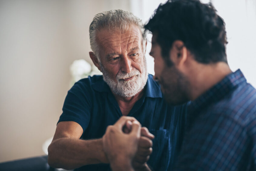 An older and a younger man clasping hands