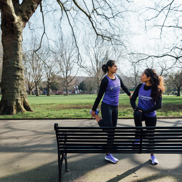 two girls stretching in a park by a bench