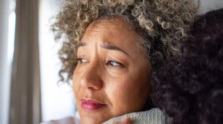 Close up of the face a woman looking concerned hugging someone else