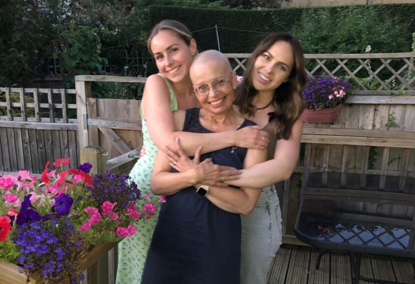 Woman with her two daughters standing outside hugging each other all smiling