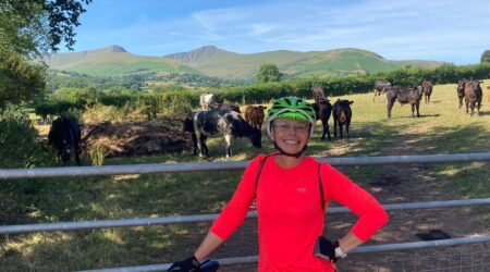 Woman smiling and holding bike and standing in front of field