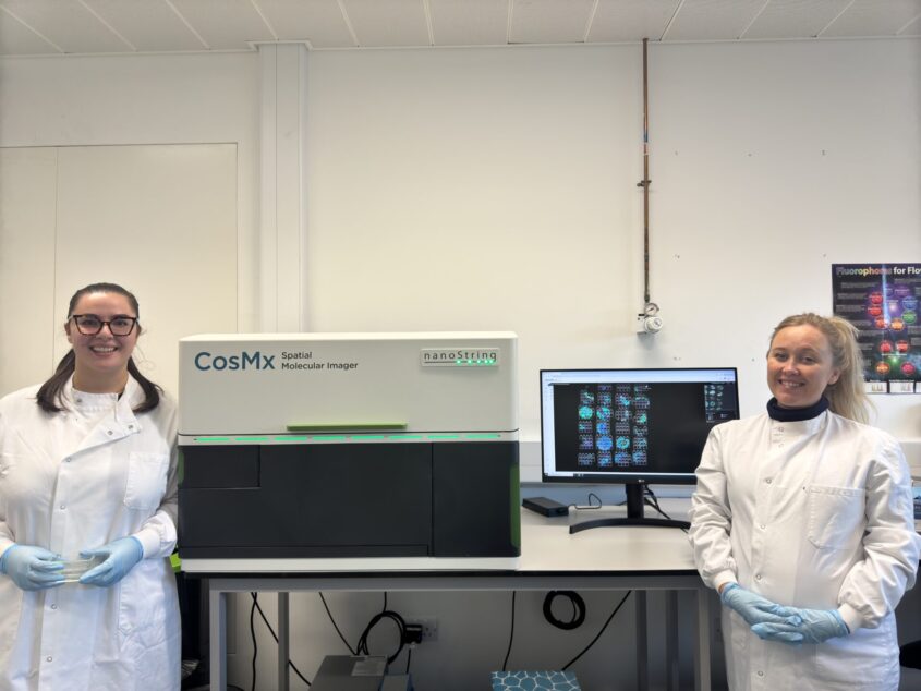 Two young researchers stand next to a machine used in this research project - a molecular imager