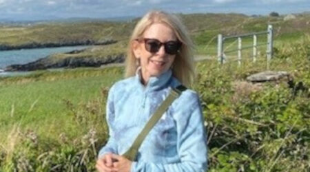 Woman wearing sunglasses standing in front of field with sea in the background.