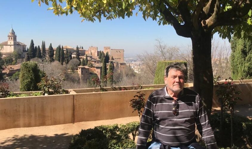 man sitting in shade of tree with a village on a hill in the background