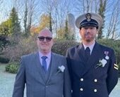 Father and son standing together outside. Son is in military uniform and the dad is dressed smartly