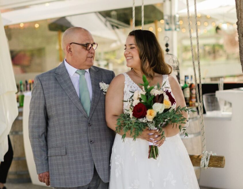 Woman in wedding dress smiling at her father who is standing by her side